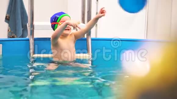 一个带着游泳眼镜的小男孩在游泳池里扔了一个蓝色的球他快乐和微笑慢动作视频的预览图
