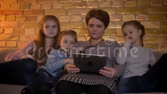 白种人母亲和女儿的家庭画像在舒适的家庭氛围中用心观看平板电脑视频的预览图