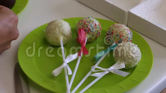 一个女人在盘子里装饰辫子蛋糕的蝴蝶结用不同颜色的糖果装饰在吉夫的盒子附近视频的预览图