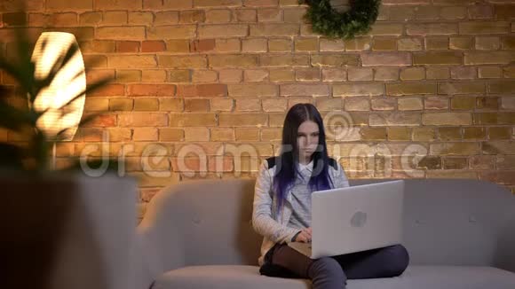年轻漂亮的白种人女性在笔记本电脑上观看视频坐在沙发上微笑的特写镜头视频的预览图