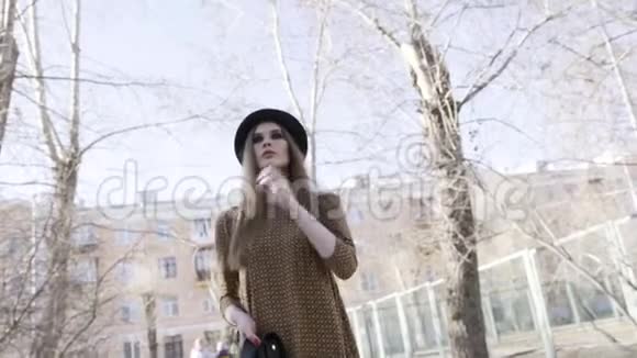 时尚的漂亮女人抚摸着她的头发穿着黑色皮夹克和帽子在户外散步视频的预览图