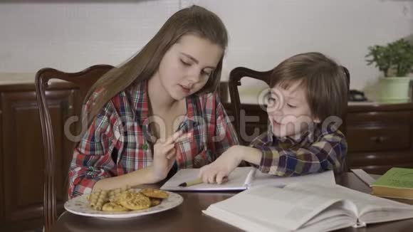 姐姐和弟弟一起做作业坐在家里的桌子旁十几岁的女孩在帮助小女孩视频的预览图