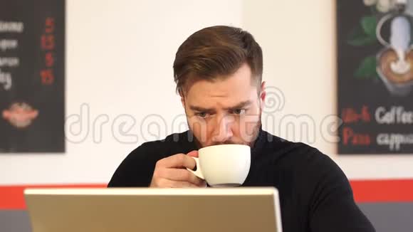 一位留胡子的年轻商人在咖啡店的肖像他在笔记本电脑上工作视频的预览图