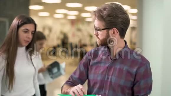 画像一个戴着眼镜穿着休闲格子衬衫留着销售报告的人站在大厅里看文件视频的预览图