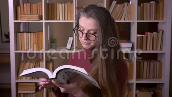 年轻的白种人女学生戴着眼镜看着一本书开心地笑着看着摄像机视频的预览图