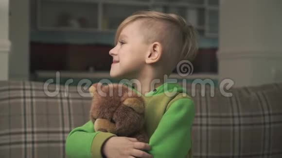 一个穿着睡衣的小男孩抱着一只泰迪熊站在客厅里的肖像快乐视频的预览图