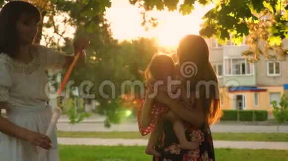 妈妈和她的女儿在日落时在傍晚的城市公园吹大肥皂泡孩子们和妈妈一起玩一起笑视频的预览图