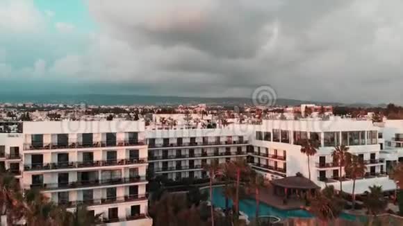 日落时酒店和建筑物的鸟瞰图空中无人机射击酒店游泳池和棕榈视频的预览图