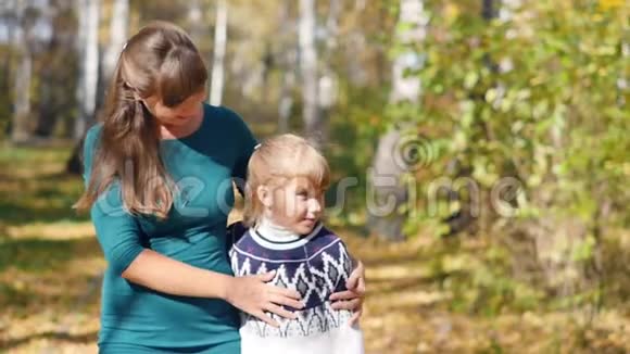 快乐的年轻母亲和她的小红发女儿一起在一个秋天的公园里散步他们笑着玩视频的预览图