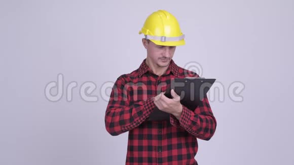 快乐胡子男建筑工人在剪贴板上阅读指导视频的预览图