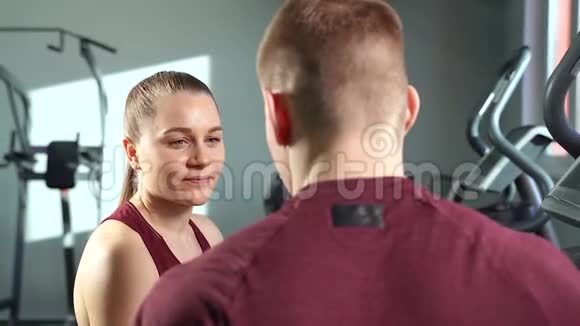 一位微笑的年轻女子在健身房和教练交谈的肖像视频的预览图