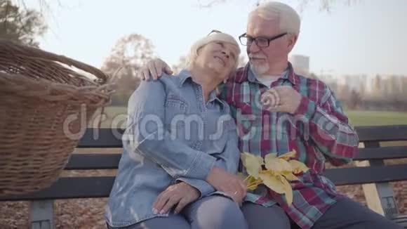 微笑的白种人退休家庭坐在长凳上在阳光下交谈成熟的欧洲夫妇阳光明媚视频的预览图
