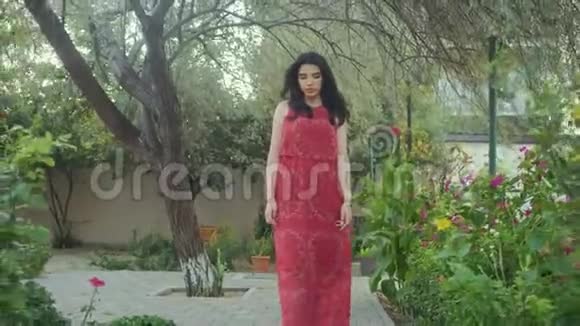 穿着红衣服的美丽女孩独自在绿色的花园里漫步视频的预览图