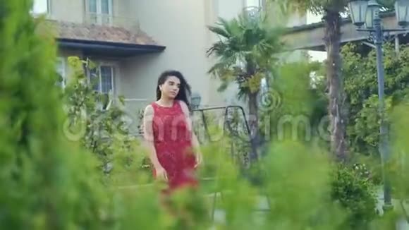 穿着红衣服的美丽女孩独自在绿色的花园里漫步视频的预览图