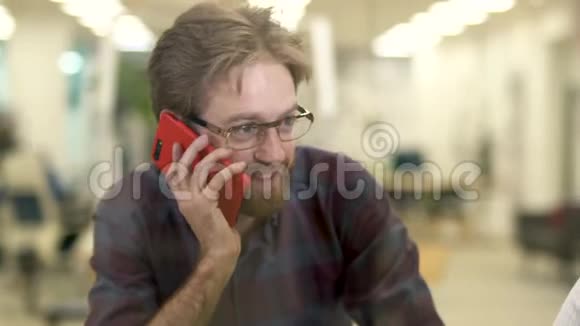大胡子带着眼镜和休闲格子衬衫的微笑男人在手机上说话坐在桌子旁的一个女孩视频的预览图
