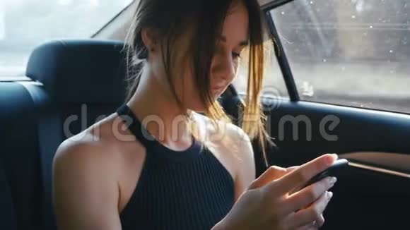肖像年轻女子在与司机一起乘坐汽车时使用智能手机女孩正在检查指甲聊天视频的预览图