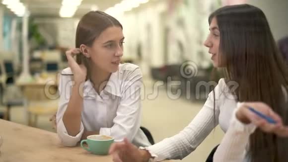 坐在桌子旁的两个女孩吻了那个留着眼镜和一件休闲格子衬衫的胡子的合适男人朋友花钱视频的预览图