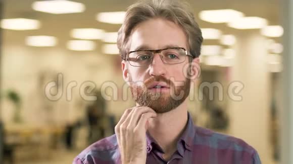 一幅年轻迷人的戴着眼镜穿着休闲格子衬衫留着胡须的严肃男人的肖像全神贯注地面对着一个难题视频的预览图