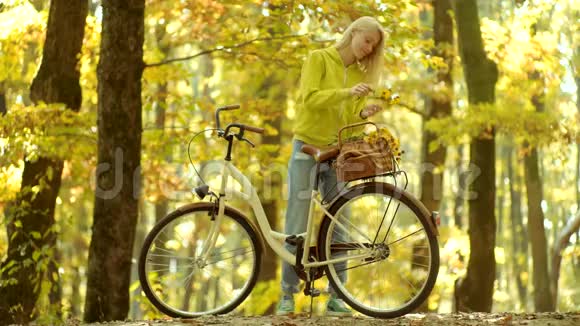 女孩们抱着带花篮的旧自行车车把公园里骑自行车的漂亮年轻女人无忧无虑的女人秋天视频的预览图
