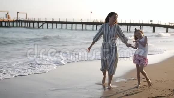 日落时分母亲和小女儿一起在沙滩上散步度假的幸福家庭视频的预览图