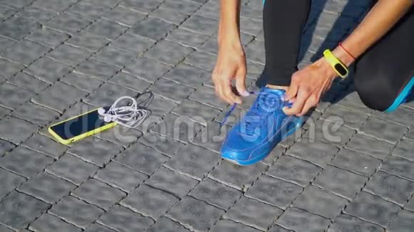 女跑步者用智能手表和智能手机准备跑步鞋的特写视频的预览图