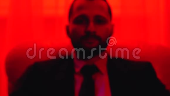 有胡子的男人坐在椅子上向前倾斜的肖像在红灯下射击视频的预览图