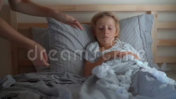 一个生病的小男孩躺在床上妈妈吻他测量他的体温婴儿流感概念视频的预览图