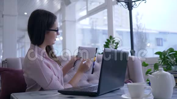 智能漂亮的女孩在电子学习视频聊天在现代上网本显示记事本与笔记和微笑坐在一个视频的预览图