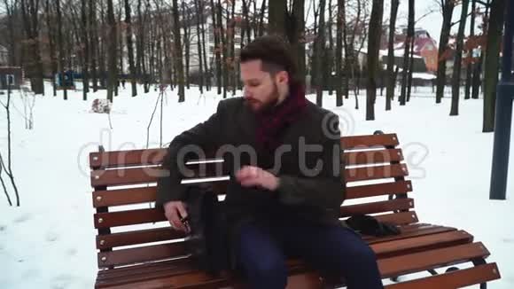 在冬天的公园里一个长胡子的人坐在草地上商人打开箱子拿书视频的预览图