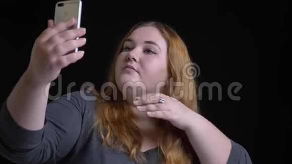 年轻的超重白种人女性的特写镜头她的头发是金色的黑发在电话里自拍视频的预览图