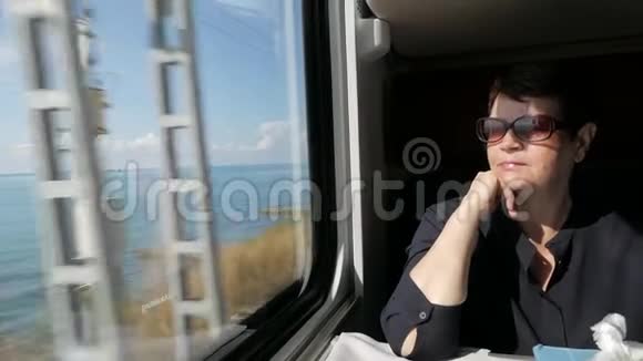 一位身穿黑色衬衫戴墨镜坐在火车车厢窗户附近的老妇人视频的预览图