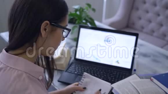在电子教育期间学生女孩坐在咖啡馆的笔记本电脑旁一边用书在线学习课程视频的预览图