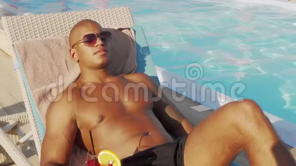 英俊的非洲男人在泳池边喝日光浴视频的预览图