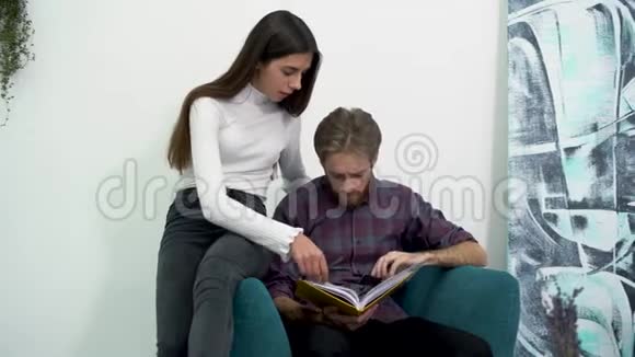 两个年轻漂亮的女孩和英俊的胡须男正坐在椅子上看书轻松的休闲办公室视频的预览图