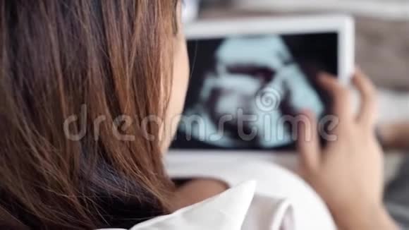 美丽的年轻孕妇躺在床上用数字平板电脑看婴儿的超声波视频的预览图