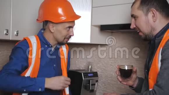 两名穿着工作服和戴着防护头盔的男子在休息时在厨房喝着煮好的咖啡视频的预览图