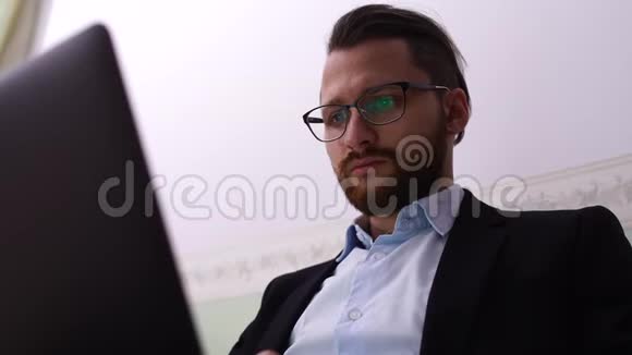 一幅英俊的男人带着眼镜在笔记本电脑上打字的肖像留胡子的商人在家工作视频的预览图