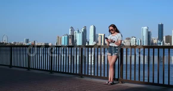 大城市和海湾背景下的女孩戴着一部太阳镜的智能手机视频的预览图