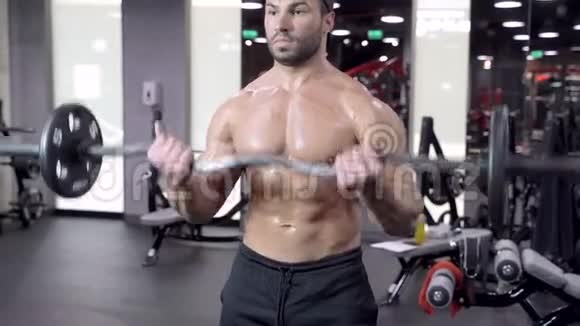 肌肉男在健身房锻炼用杠铃做运动强壮的男性裸露的躯干腹肌视频的预览图