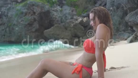 美丽的女人穿着比基尼躺在沙滩上的蓝海和悬崖景观迷人的女人在沙滩上放松视频的预览图