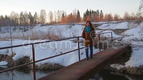一位年轻的红发女子在日出时沿着桥过一条小河视频的预览图