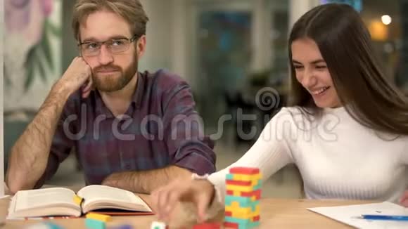 一群朋友坐在桌旁玩木积木塔戴眼镜的留胡子的人先观察然后观察视频的预览图