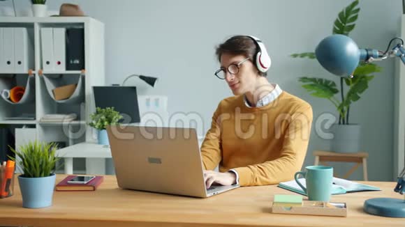 戴耳机的帅哥正在现代办公室工作时听音乐视频的预览图