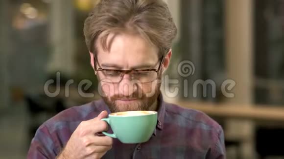一个戴着眼镜带着笑容的留胡子的家伙喝着咖啡享受的肖像视频的预览图