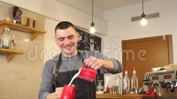 一个男咖啡师在咖啡店的肖像他把牛奶从杯子倒到杯子视频的预览图