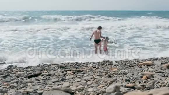 爸爸和儿子在石滩上的暴风雨中在海浪中游泳后景视频的预览图