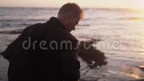 背面的男子背包站在海滩上观看美丽的金色日落慢动作视频的预览图