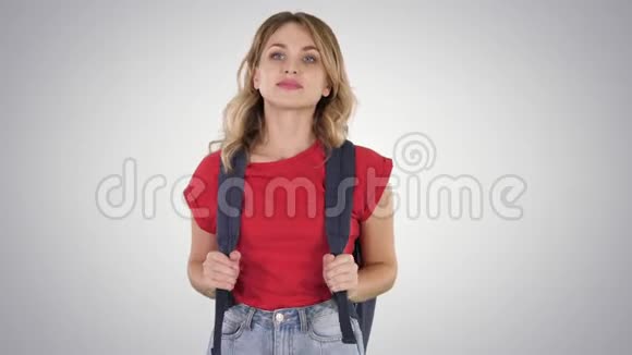 年轻漂亮的女人穿着休闲T恤背包和牛仔裤走在梯度背景上视频的预览图
