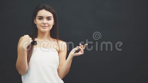 站在黑色背景上的年轻漂亮女孩同时画笔正在脸上微笑视频的预览图