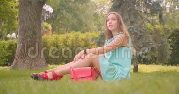年轻的长发美丽的女性坐在草地上在公园里快乐地休息视频的预览图